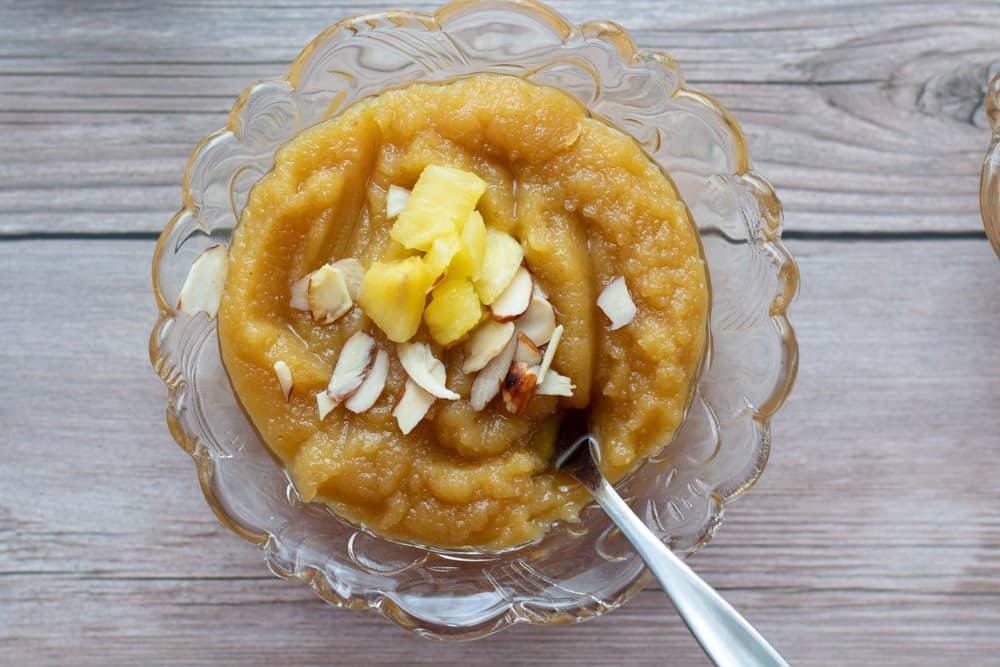 Almond pineapple halwa served in a glass bowl with a dessert spoon with pineapple and almond pieces on top