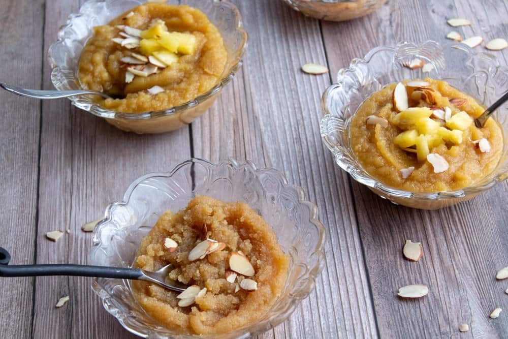 Almond pineapple halwa served in 2 glass bowls with dessert spoons with pineapple and almond pieces on top and plain almond halwa served in 2 glass bowls with dessert spoons and sliced almonds on top.