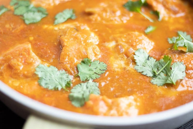 Close up image of Tomato coconut salmon curry Indian style in a pan.