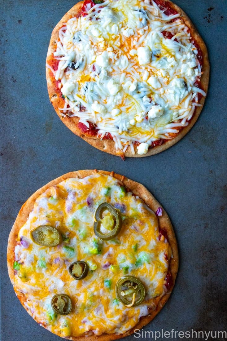 Greek Inspired Pita Pizza and Mexican Inspired Pita Pizza after baking on a sheet pan.