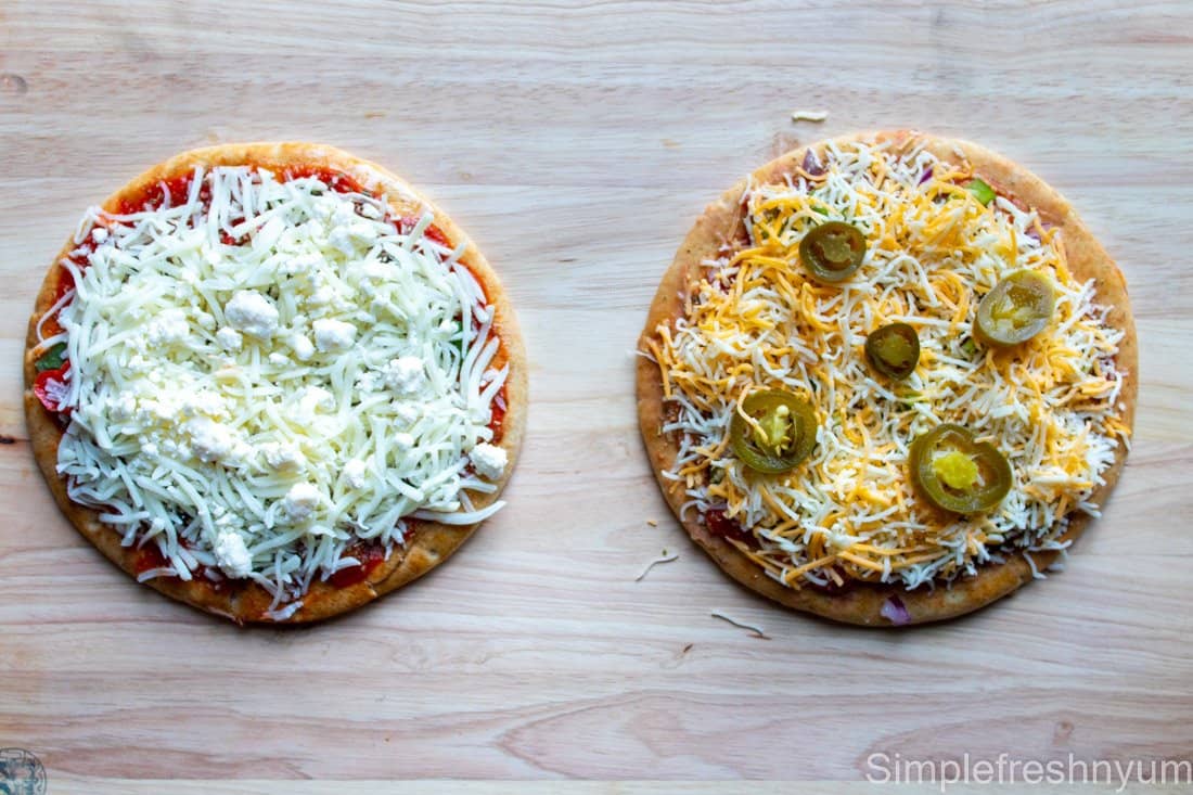 Greek Inspired Pita Pizza and Mexican Inspired Pita Pizza in the middle of the prep after putting cheese on them to cook.