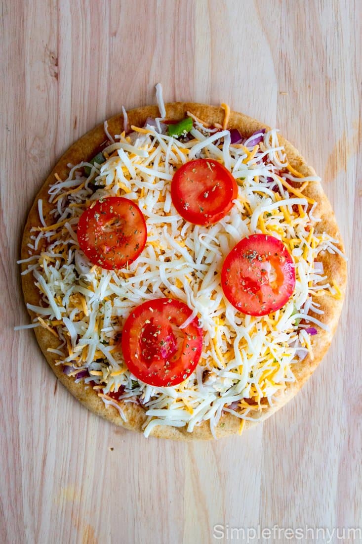 Vegetable Pita pizza ready to bake on a wooden cutting board