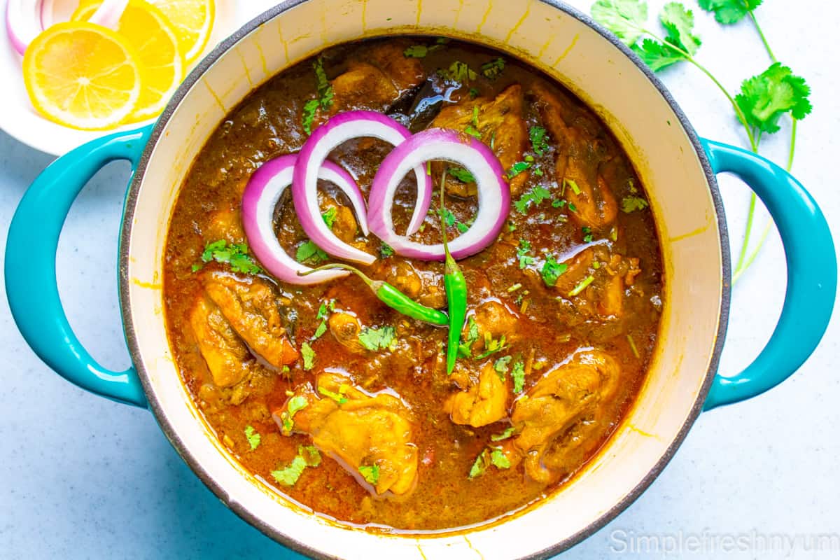 Picture of Chicken palak curry finished in the blue dutch oven pot with onions cut into rings, cilantro and green chili on the top.