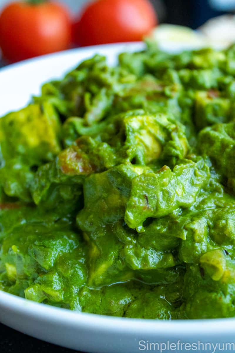 Close up image of Palak paneer curry on a white plate with whole red vine tomatoes in the back ground.