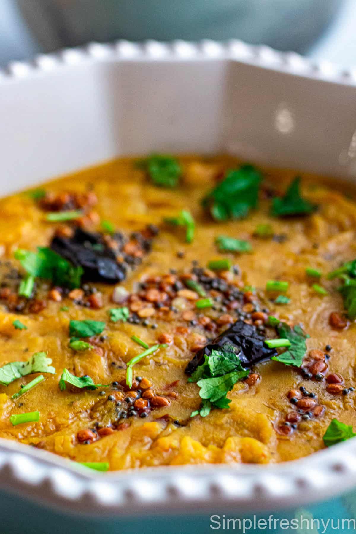 Close up image of Masoor dal served in a white serving dish with tempering on top