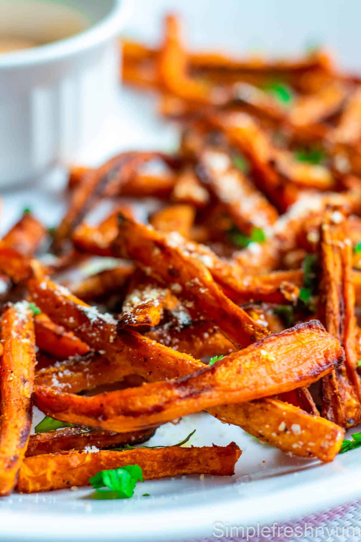 Close up image of carrot fries made in air fryer served on a white plate with parmesan cheese and cilantro sprinkled on top.