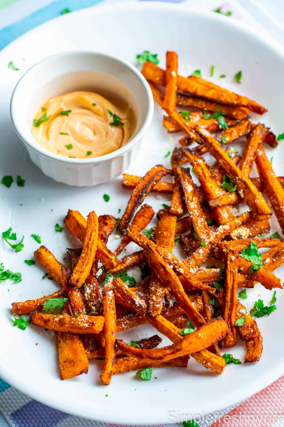 Carrot fries served in a white oval serving plate with parmesan cheese and chopped cilantro sprinkled on top. Sriracha greek yogurt dip is served on the side in a small round white bowl.