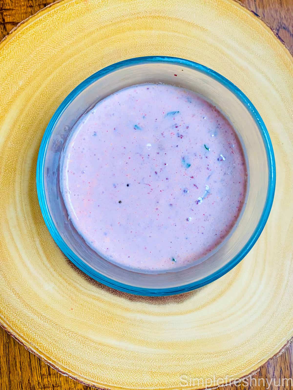 cranberry chutney mixed with plain yogurt served in a round glass bowl on a light coloured wooden board.