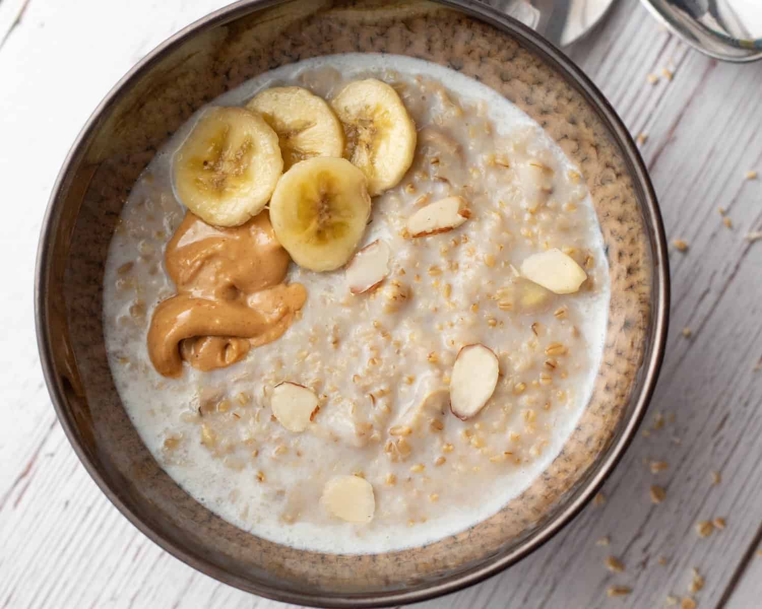 Creamy banana steel cut oatmeal in a bowl topped with banana slices, sliced almonds and peanut buter