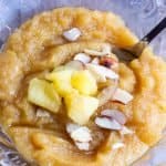 Badam pineapple halwa served in a glass bowl with a dessert spoon and pineapple and almond pieces on top
