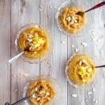 Badam halwa plain and badam halwa with pineapple is served in 4 bowls altogether with spoons in each bowl and sliced almonds are scattered on the background surface.