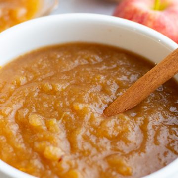 Apple sauce in a white serving dish with cinnamon stick dipped in it.