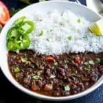 Black bean soup served with white rice with jalapeno slices and a lemon wedge on the side
