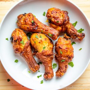 Crispy chicken legs on a white plate on a wooden surface with cilantro garnished in top.