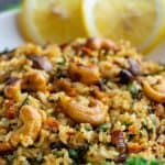 Close up image of Kale rice with cashew nuts garnished on top served on a white plate.