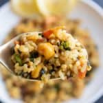 Close up image of Kale rice on a spoon with a white plate full of kale rice in the back ground.