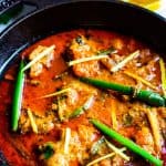 Chicken Karahi served in a black cast iron wok ( Karahi) with slices of jalapenos and ginger juliennes on the top