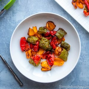 Bell peppers roasted in air fryer served in a white round plate with a fork and green tongs on the side.