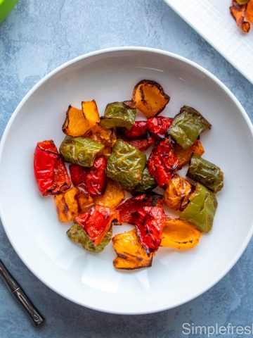 Bell peppers roasted in air fryer served in a white round plate with a fork and green tongs on the side.