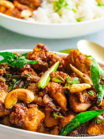 Close up image of South Indian style chicken stir fry served in a white oval serving dish with cilantro garnished on top.