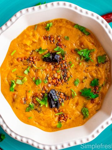 Masoor Dal served in a white serving bowl with tempering on top and cilantro garnished on top.