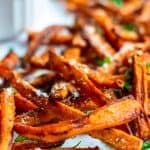 Close up image of carrot fries made in air fryer served on a white plate with parmesan cheese and cilantro sprinkled on top.