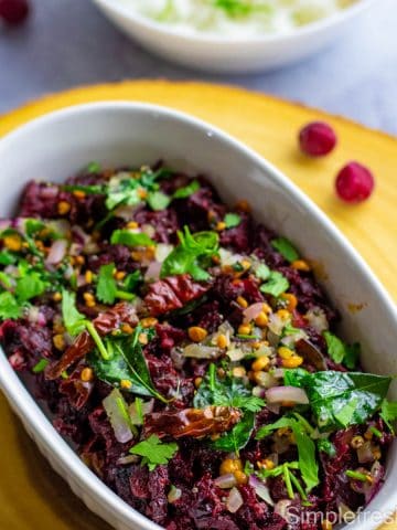 Indian cranberry chutney is served in a white oval dish with tempering on the top. Serving dish is placed on a light colored wooden board and cranberries are strewn around the serving dish.